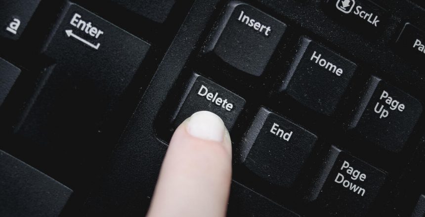 Finger over the delete key from a dusty black keyboard.